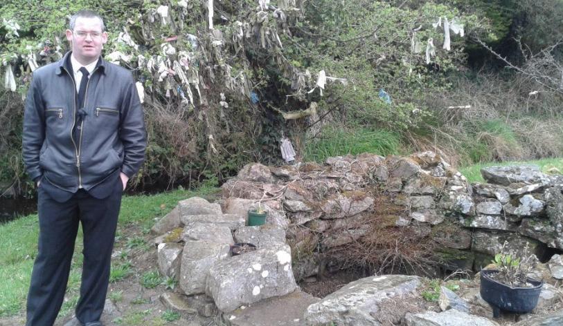 Tomás Ó Cárthaigh at Tubberpatrick well, with rags on the Fairy Tree in the background