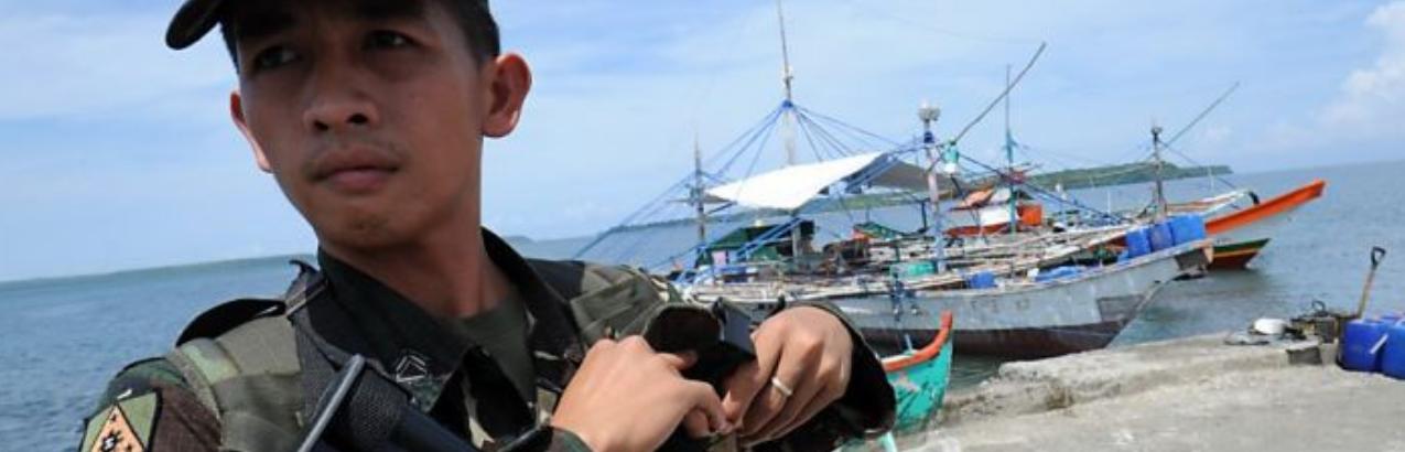 A Philippine soldier stands guard next to fishing boats (back) at a pier in Masinloc town, Zambales province, 230 kilometres (140 miles) from Scarborough Shoal on May 18, 2012, the conflict, a cold war of sorts, is still ongoing today with China invading waters of the Phillipines and Vietnam
